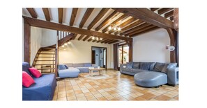 A spacious living room with a high ceiling, exposed wooden beams, a blue sofa, a grey sofa, and a tiled floor. - Charming family home in Normandy (Chamblac)