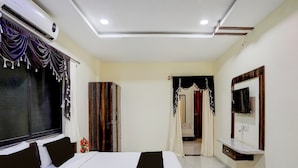 A bedroom with a bed, a wardrobe, a TV, and a window with curtains. - Classic With Balcony Daulatabad Fort Aurangabad (Chhatrapati Sambhajinagar)