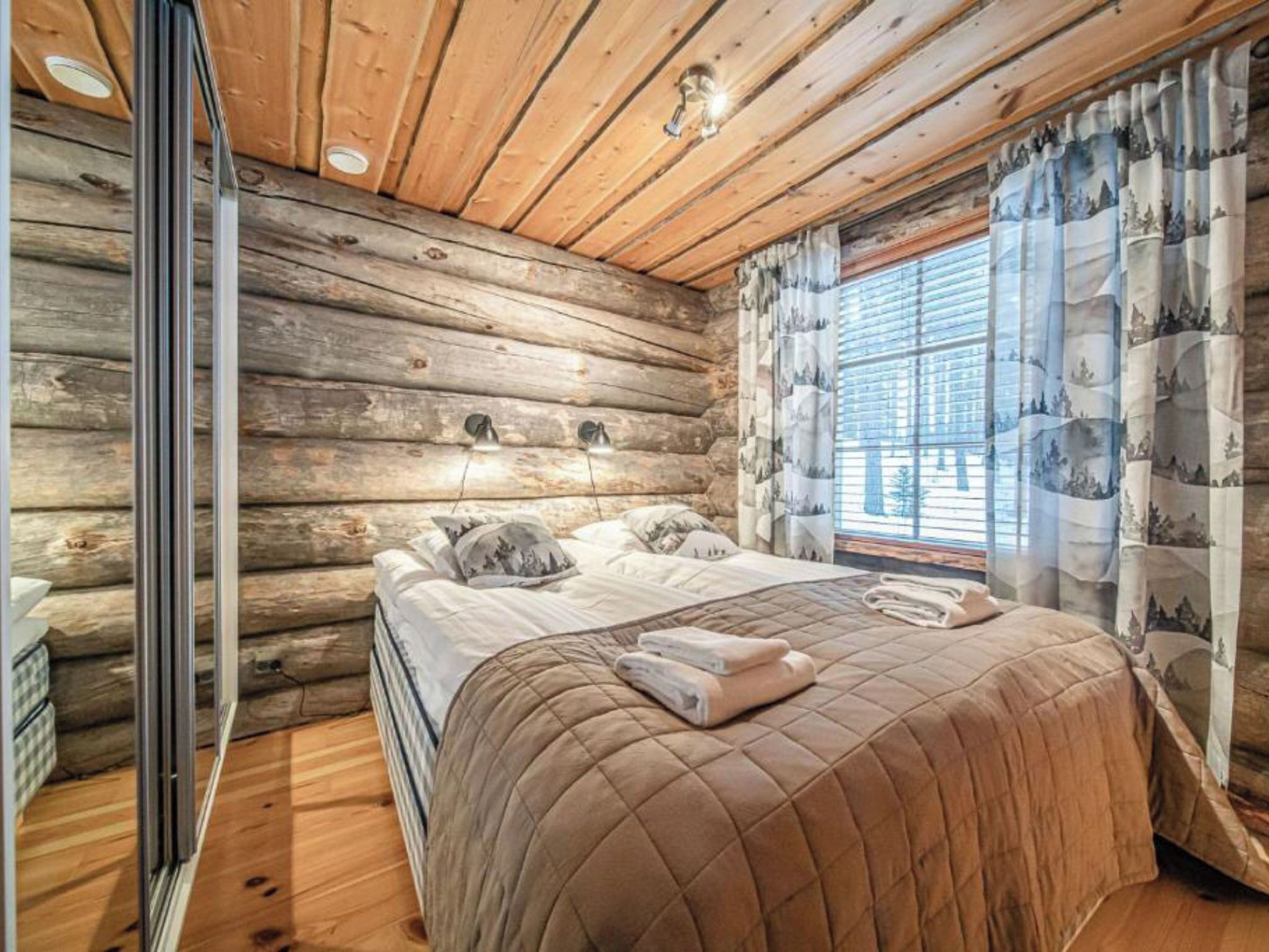 A log cabin bedroom with a bed, pillows, and a window with curtains.