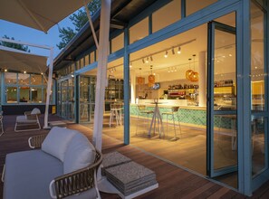 Un área de bar moderna al aire libre con terraza de madera, asientos y barra.
