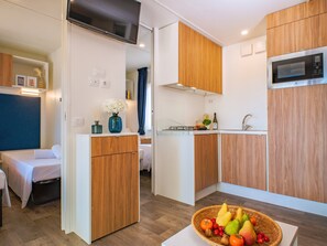 Cocina compacta con armarios de madera, microondas y comedor con mesa y sillas.