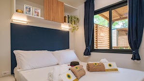 Ein Hotelzimmer mit Bett, Kissen, Kopfteil, einem Fenster mit Vorhängen, einem Nachttisch und Handtüchern mit einem Logo.
