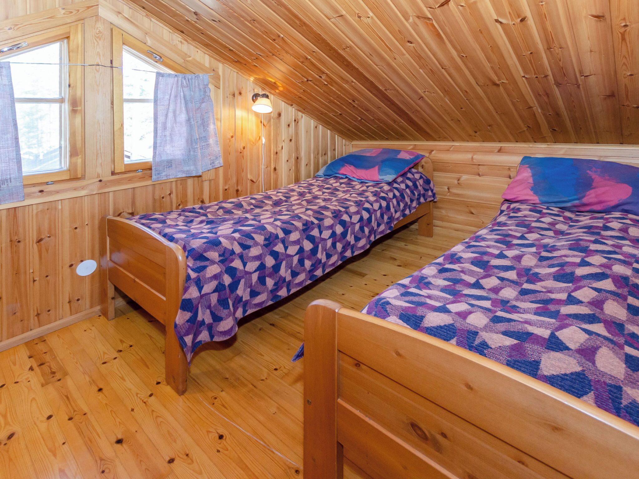 A wooden cabin with two beds, a window with curtains, and a lamp.