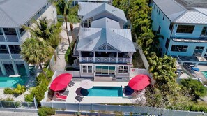 A large house with a pool, two red umbrellas, and a covered patio area. - Waves Edge - Beachfront! (Anna Maria)