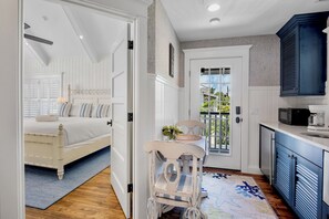 A bedroom with a bed, a chair, a table, and a door leading to a balcony. - Waves Edge - Beachfront! (Anna Maria)