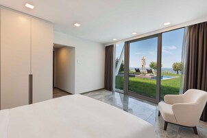 Una habitación de hotel moderna con una cama grande, una silla y vistas a una piscina y follaje.