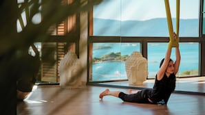 A person performing aerial yoga with a view of the ocean and mountains through large windows. - Vitalica Wellness Bodrum (Bogazıcı)