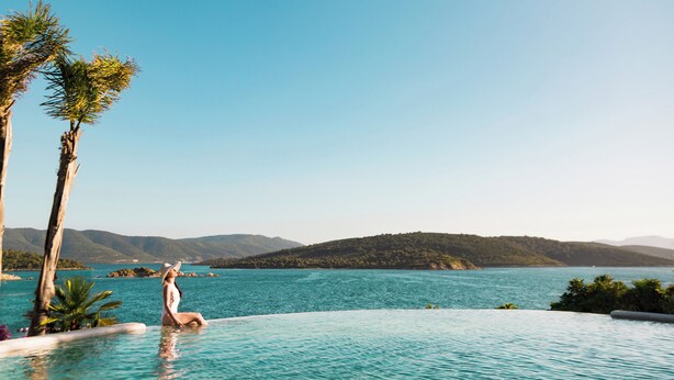 A person sitting by a pool with a view of a lake and mountains. - Vitalica Wellness Bodrum (Bogazıcı)