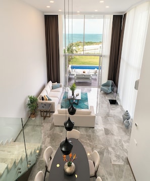 Een moderne woonkamer met een glazen trap, een eethoek met een vaas, en uitzicht op de oceaan.