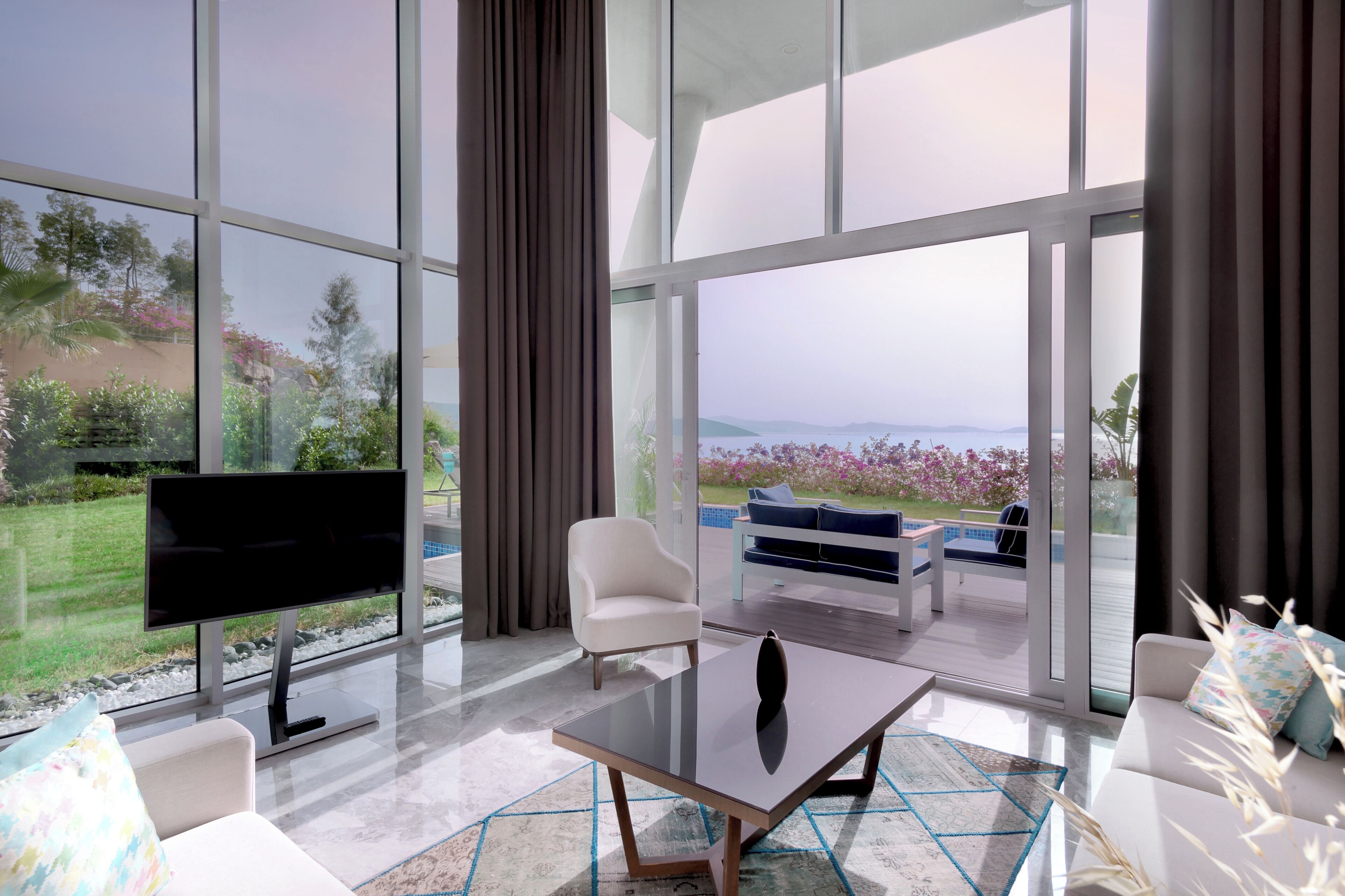 Una sala de estar moderna con un televisor grande, asientos cómodos y vistas a una piscina y jardín.