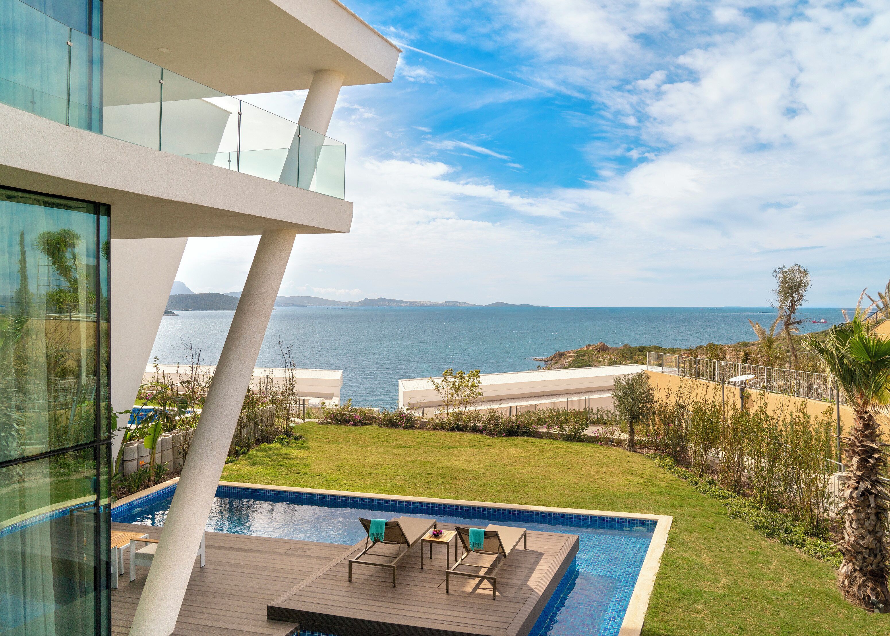 A modern building with a pool area, including lounge chairs and a wooden deck.
