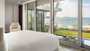 A modern hotel room with a large bed, a chair, and a view of the sea and pool. - Vitalica Wellness Bodrum (Bogazıcı)