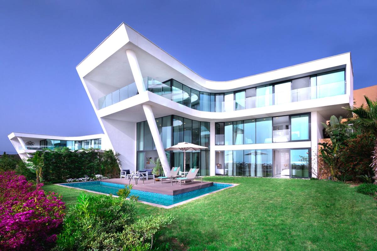 Una casa moderna con piscina, mobiliario de exterior y abundante vegetación.