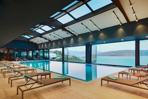 Uma  área à beira da piscina com espreguiçadeiras, vista para o mar e teto com claraboias.