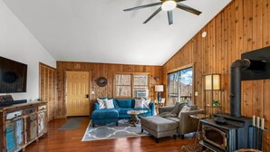 A cozy cabin interior with wooden walls, a sofa, a chair, a table, a fireplace, and a ceiling fan. - Cardinals Nest In The Smokies ~ Family Friendly (Haywood County)