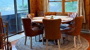 A wooden-paneled dining room with a round table, leather chairs, and a view of the outdoors. - Cardinals Nest In The Smokies ~ Family Friendly (Haywood County)