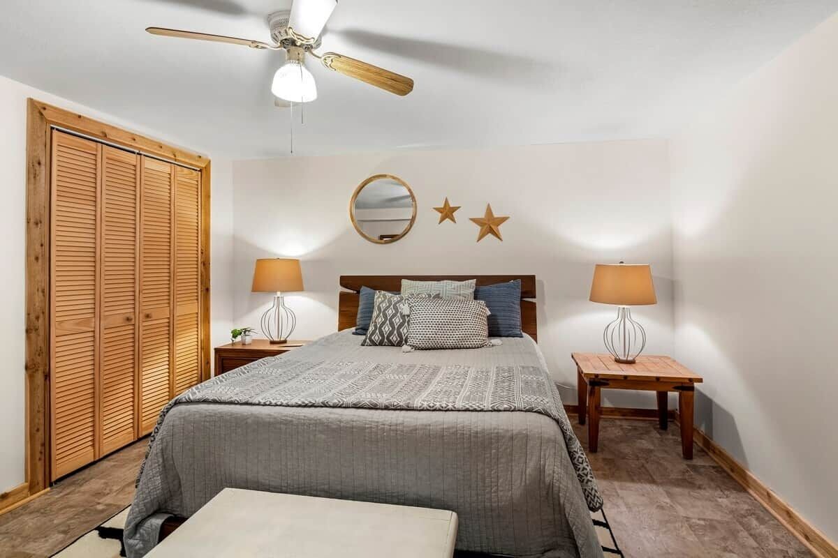 Une chambre à coucher avec un lit, deux tables de chevet avec des lampes, une armoire en bois, un ventilateur de plafond et un mur orné d’un miroir et de décorations en forme d’étoiles.