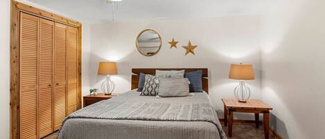 Une chambre à coucher avec un lit, deux tables de chevet avec des lampes, une armoire en bois, un ventilateur de plafond et un mur orné d’un miroir et de décorations en forme d’étoiles.