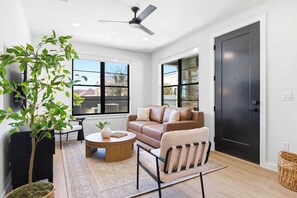A modern living room with a sofa, armchair, coffee table, and a potted plant. - Unwind in Style: Luxe Condo Getaway! (New Braunfels)