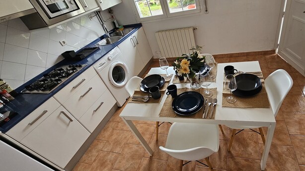 Une cuisine avec une table à manger pour deux personnes, un lave-linge et une fenêtre donnant sur un beau paysage.