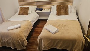 Deux lits jumeaux avec une literie beige, des oreillers blancs et des coussins décoratifs marron. Chaque lit est agrémenté d’une serviette blanche pliée.
