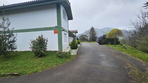Un bâtiment à la façade verte et blanche, une allée pavée et une montagne en arrière-plan.
