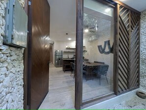 A modern interior with a stone wall, a wooden door, a dining area with a table and chairs, and a kitchen with appliances. - Private Pool + Rooftop / Stylish Tulum House for 6 (Tulum)