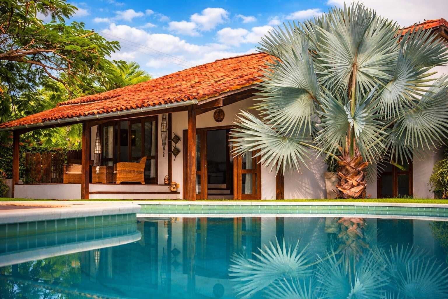 Uma casa com piscina, varanda coberta e uma grande palmeira.