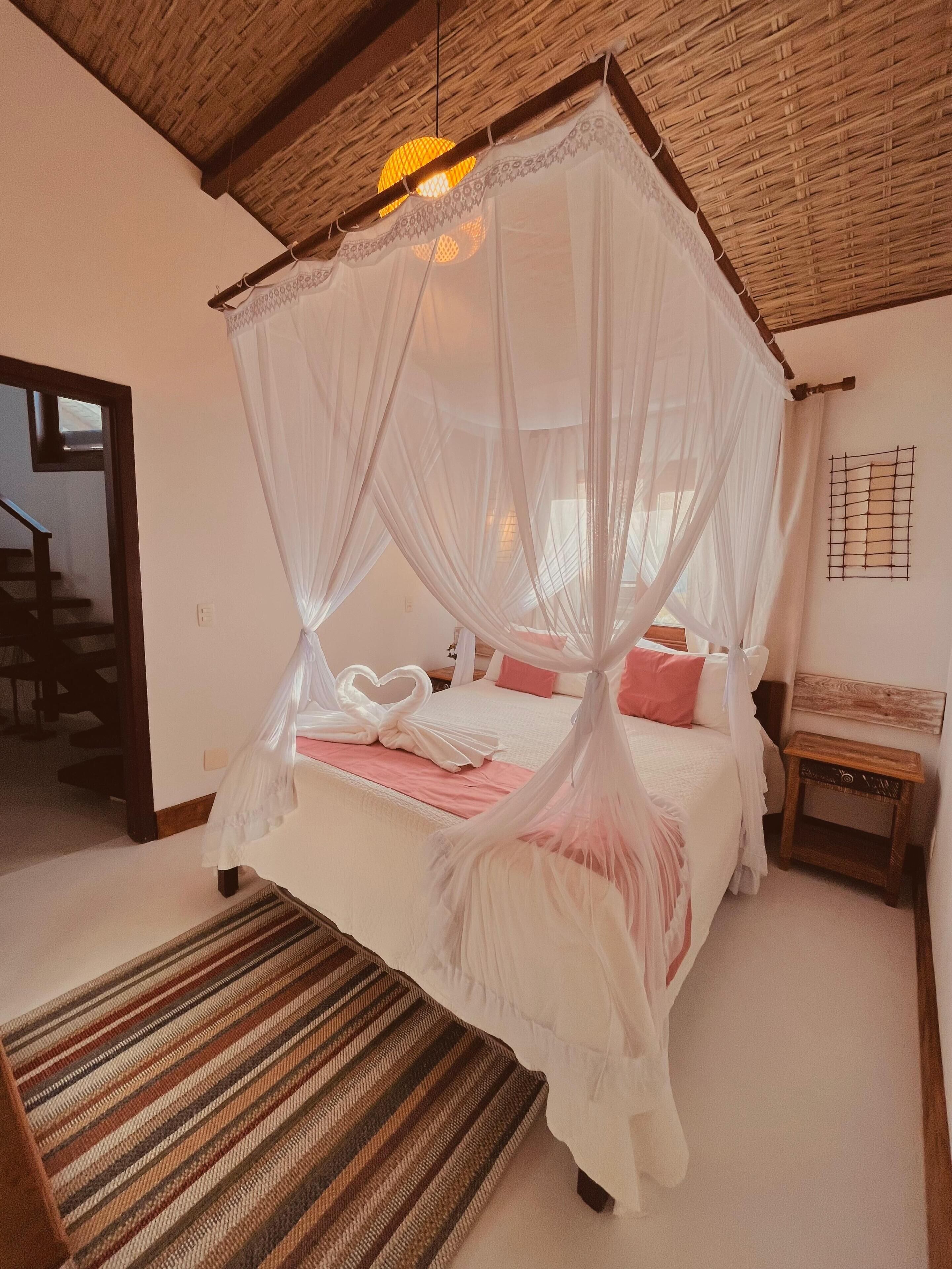 Un dormitorio con una cama con dosel, techo tejido, mesita de noche de madera y alfombra a rayas.
