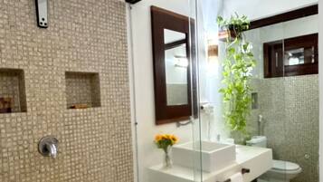 Een moderne badkamer met een douchecabine van glas, een witte wastafel en een spiegel.