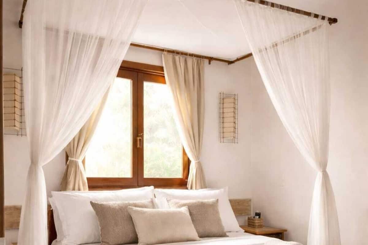 A bedroom with a canopy bed, a window with curtains, a bedside table, and a rug.