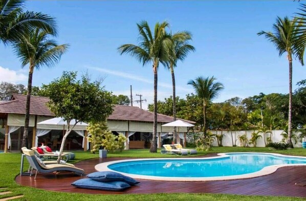 A swimming pool with lounge chairs and palm trees. - VILLA Palmeira Azul - Suíte de Charme (Porto Seguro)