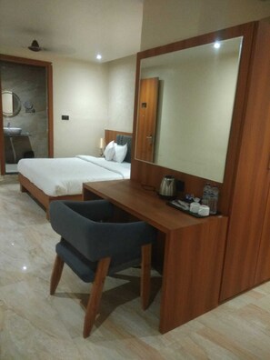 A hotel room with a bed, a desk with a mirror, a sink, and a chair. - Shreeja Central (Bhawanipatna)