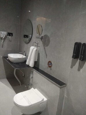 A modern bathroom with a white sink, a mirror, a towel rack, and a toilet. - Shreeja Central (Bhawanipatna)