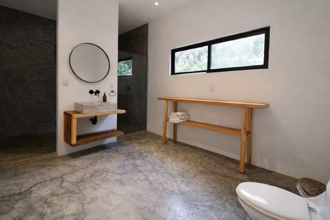 Une salle de bain avec un sol en marbre, un meuble-lavabo en bois avec un miroir, des toilettes et une fenêtre.