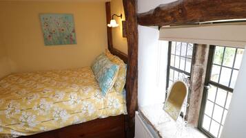 Un dormitorio con colcha estampada, cabecera de madera, lámpara de pared, ventana con vistas y radiador.