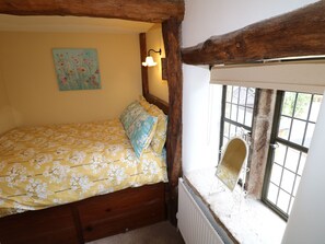 Una camera da letto con una coperta a fiori, una testiera in legno, una lampada a parete, una finestra con vista e un termosifone.