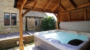 Een hottub onder een houten pergola, stenen muren en een raam met tralies.