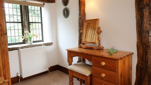 Een houten bureau met een spiegel, een radiator, een raam met uitzicht en een wandlamp.