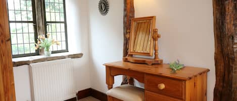 A wooden desk with a mirror, a radiator, a window with a view, and a wall-mounted light fixture.