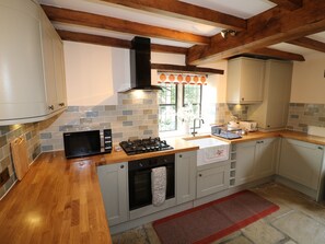 A kitchen with a microwave, stove, oven, and a window with a view of greenery. - Orchard View (Alfreton)