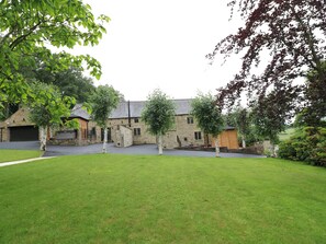 Ein Steinhaus mit Garage, umgeben von einer grünen Rasenfläche und Bäumen.