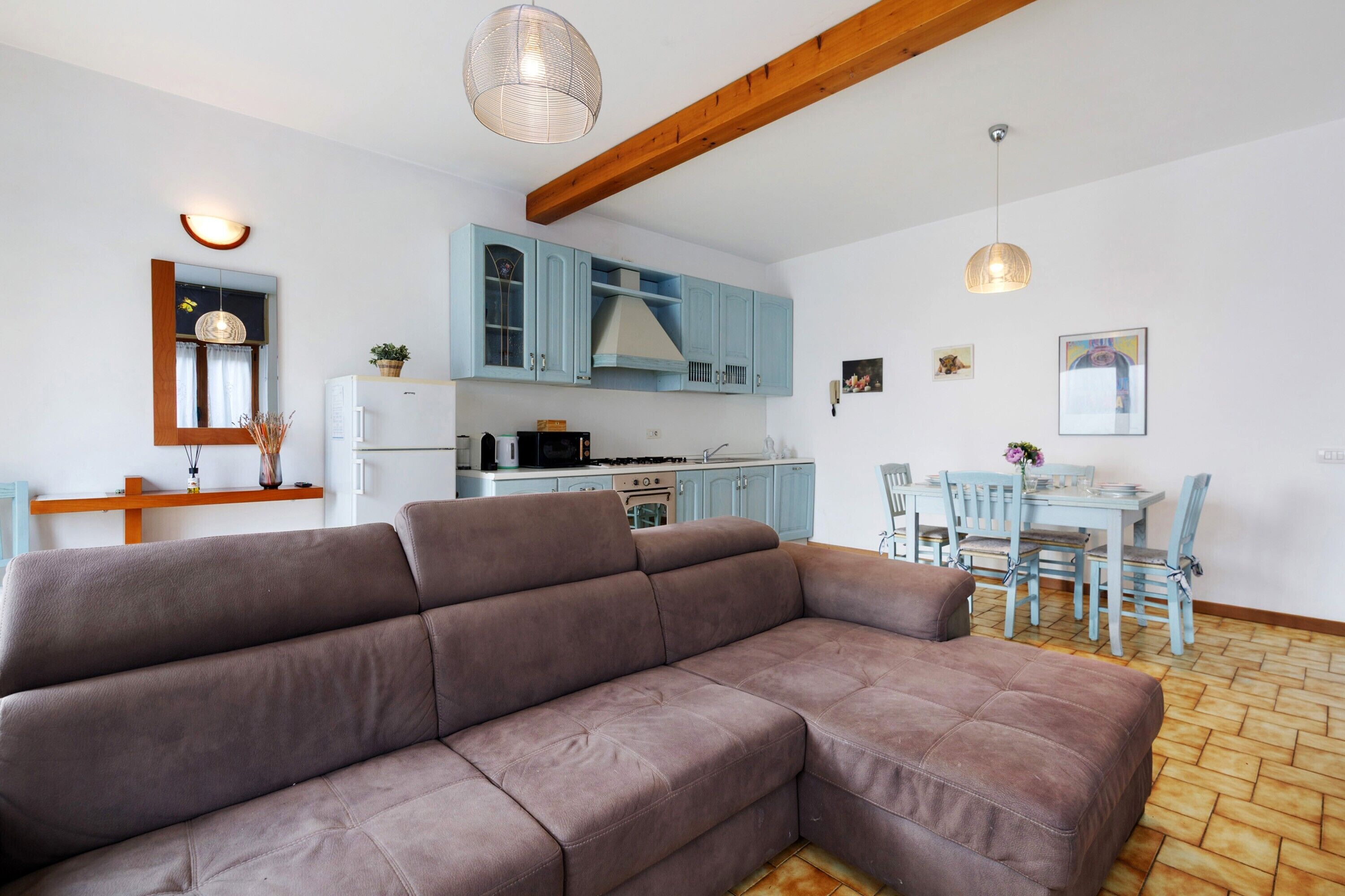 Un salon moderne avec un canapé d’angle, un coin repas comprenant une table et des chaises, et une cuisine avec des meubles de couleur bleu clair.