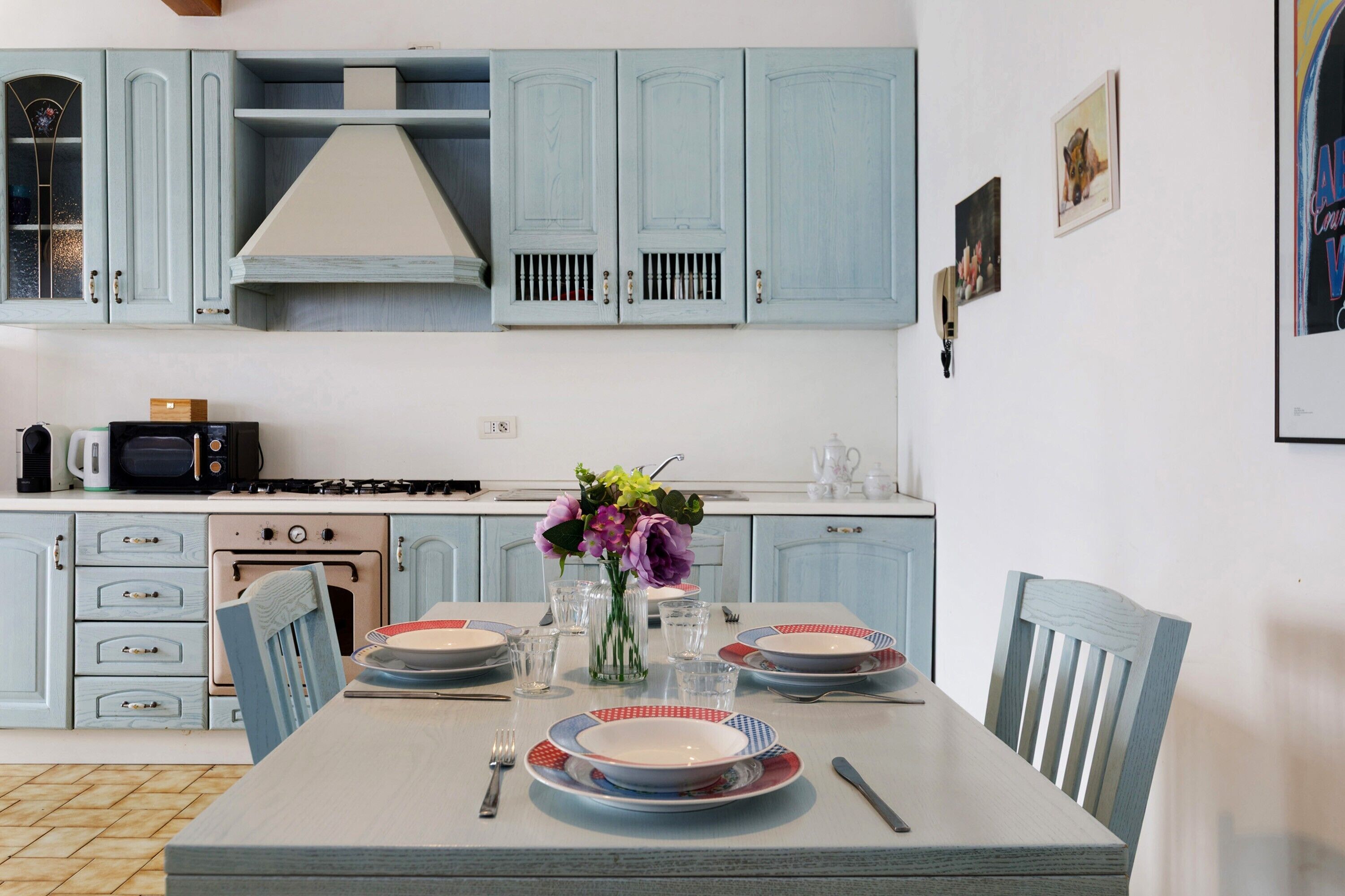 A kitchen with light blue cabinets, a dining table set with plates, glasses, and cutlery.