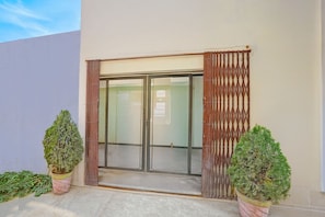 A building entrance with a sliding glass door, two potted plants, and a metal gate. - Classic Prayagraj Bus Stop Sonica Gold (Prayagraj)