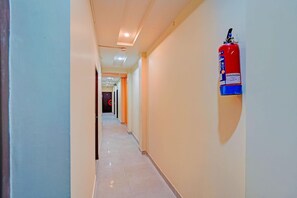 A hallway with a fire extinguisher mounted on the wall, a ceiling light, and a door at the end. - Classic Prayagraj Bus Stop Sonica Gold (Prayagraj)