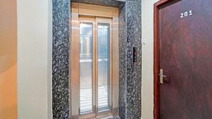 An elevator with a marble wall, a wooden door with the number 201, and a small sign indicating the floor level. - Classic Prayagraj Bus Stop Sonica Gold (Prayagraj)