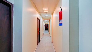 A long, narrow hallway with doors on both sides, a fire extinguisher mounted on the wall, and a ceiling light fixture. - Classic Prayagraj Bus Stop Sonica Gold (Prayagraj)