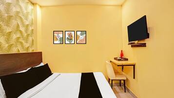A hotel room with a bed, a desk, a chair, a TV, and three framed pictures on the wall.