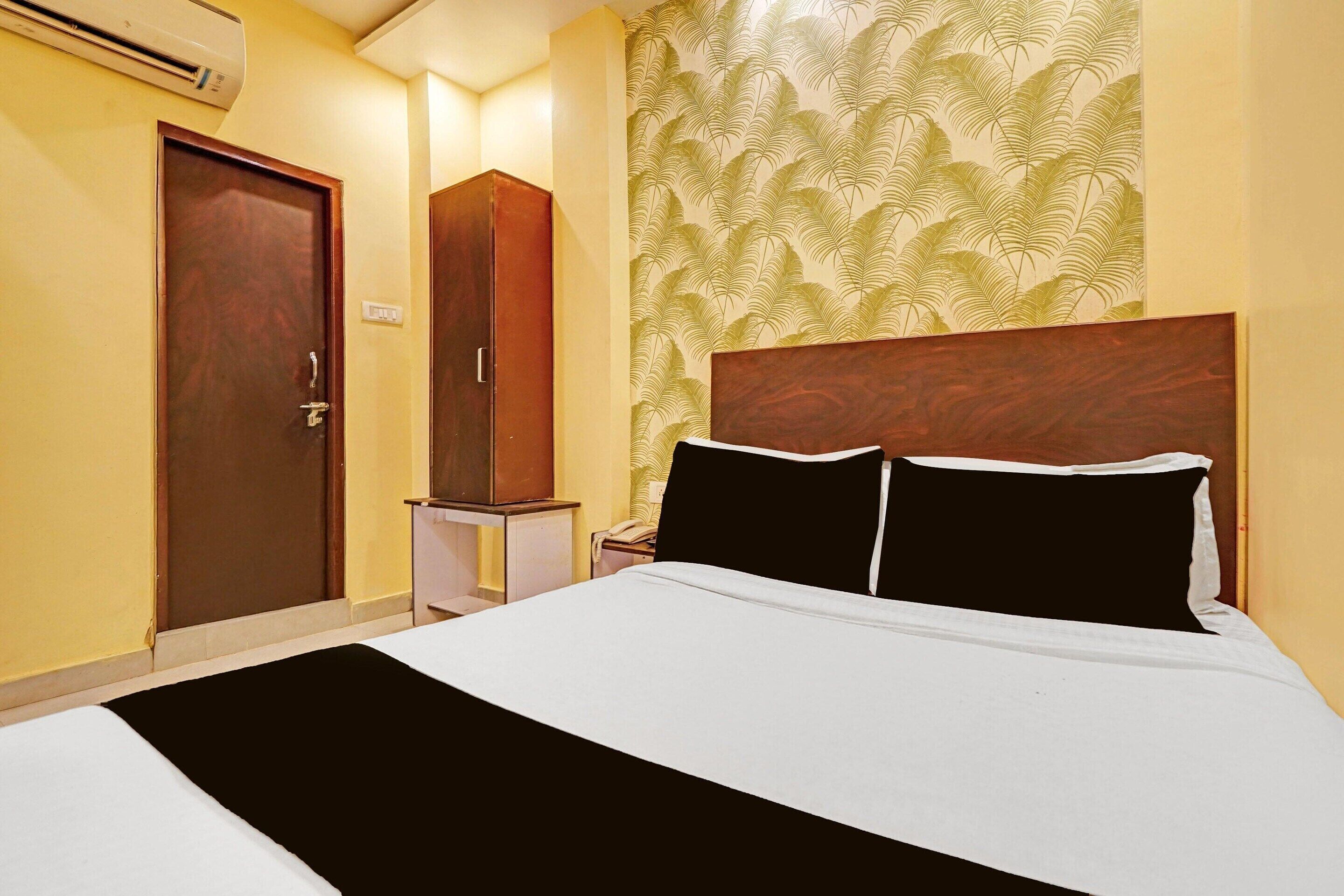 Een hotelkamer met een bed, een kledingkast, een nachtkastje en een wand met een bladmotief.
